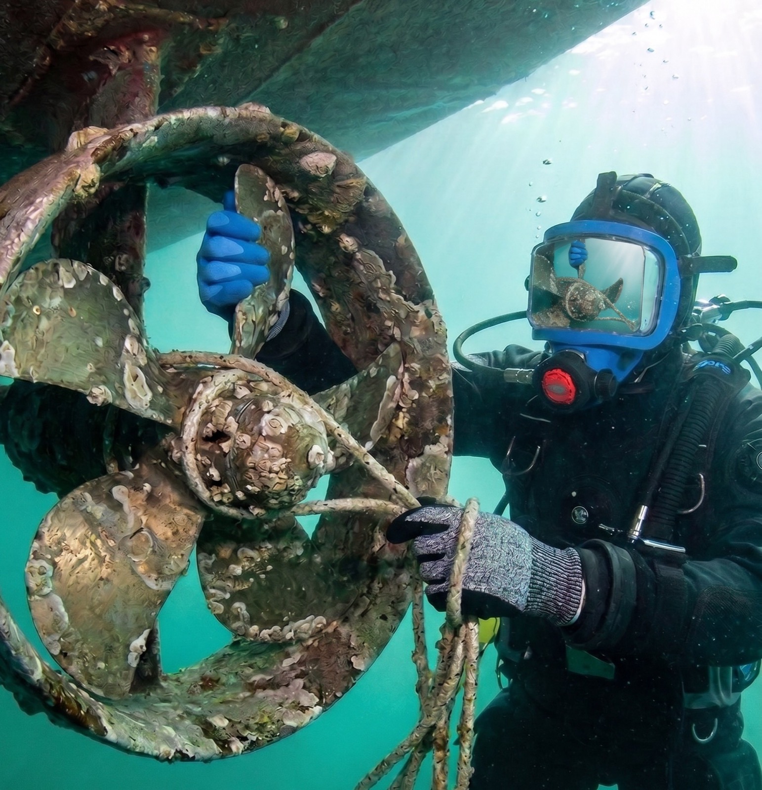 Commercial diver removing debris wrapped around a yacht propeller and shaft underwater